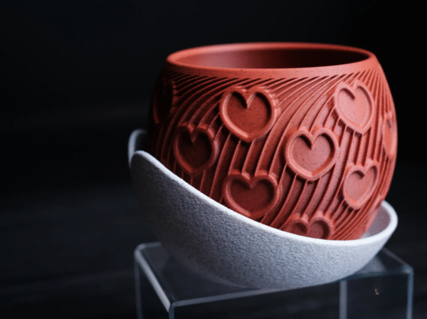 HEART – esencja uczuć w formie designu Doniczka HEART to manifest emocji zamknięty w geometrycznej perfekcji. Stworzona z myślą o wyjątkowych chwilach, stanowi niebanalny prezent dla ukochanej osoby – pełen symboliki, a zarazem absolutnie współczesny. Na powierzchni eleganckiego korpusu w odcieniu klasycznej czerwieni wyrzeźbiono rytmiczne serca, harmonijnie wtopione w dynamiczne linie przypominające strumień energii lub zakodowane wyznanie. To coś więcej niż doniczka – to designerski artefakt, który celebruje uczucie w jego najczystszej formie. Osadzona w kontrastującej, teksturalnej podstawce, HEART zyskuje charakter obiektu galeryjnego, a nie tylko użytkowego. Doskonała na Walentynki, rocznicę, dzień zaręczyn lub jako intymny gest bez okazji. Dostępna w wymiarach: 130 × 130 × 100 mm (szerokość × głębokość × wysokość) Podaruj coś, co nie zwiędnie. HEART – design, który mówi „kocham” bez słów.